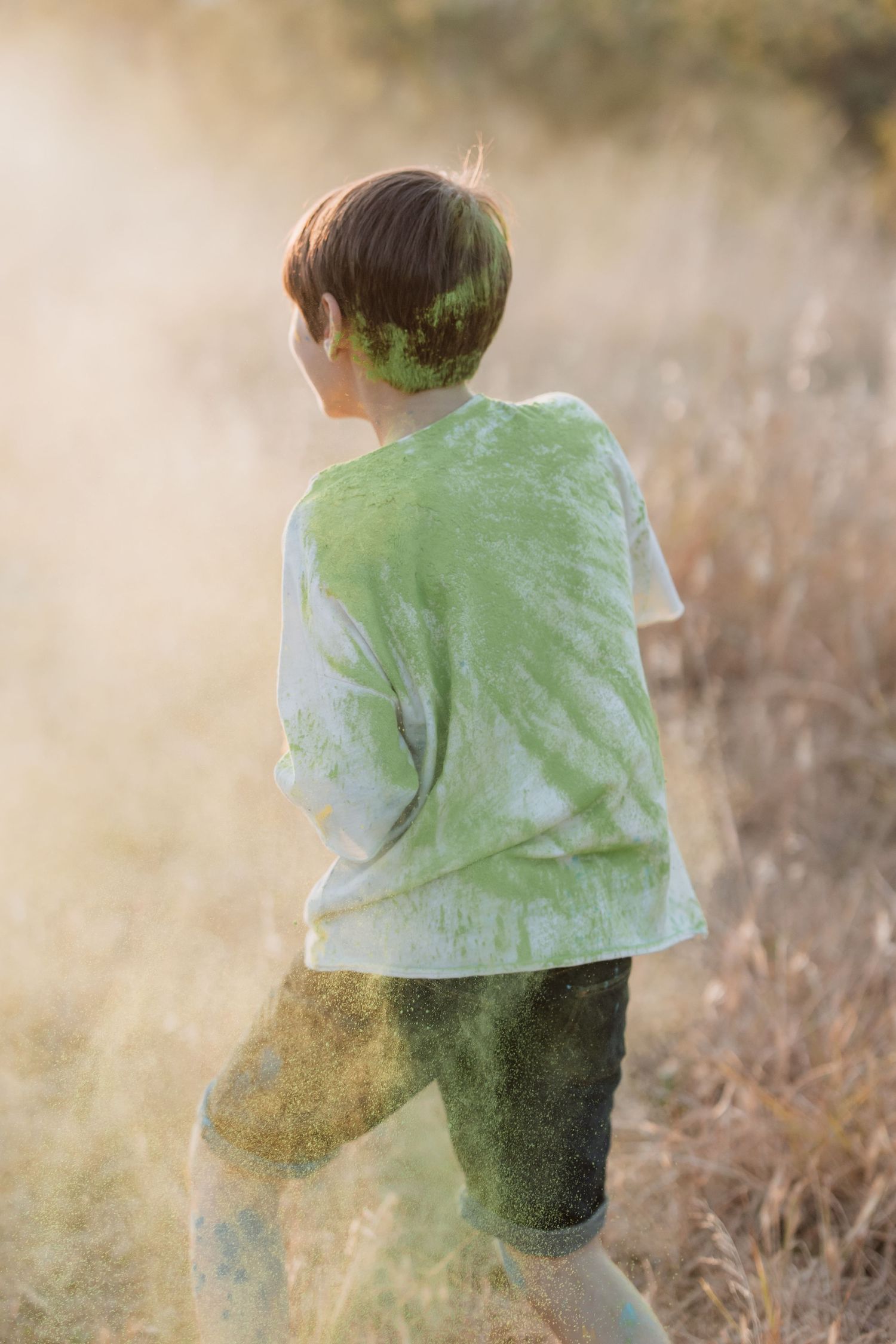 Silhouetted figure in a light green shirt stands in golden sunlit field during magic hour with dreamy backlit atmosphere.