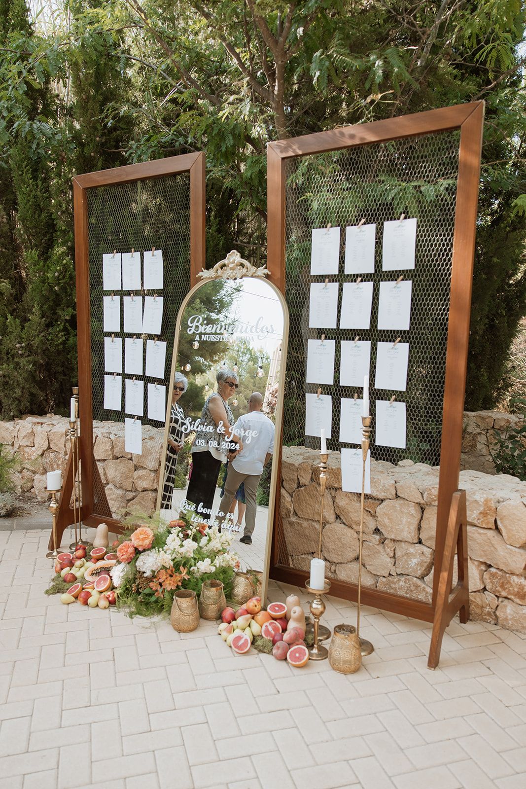 Wedding seating chart display with wooden frames, mirror, and floral decorations.