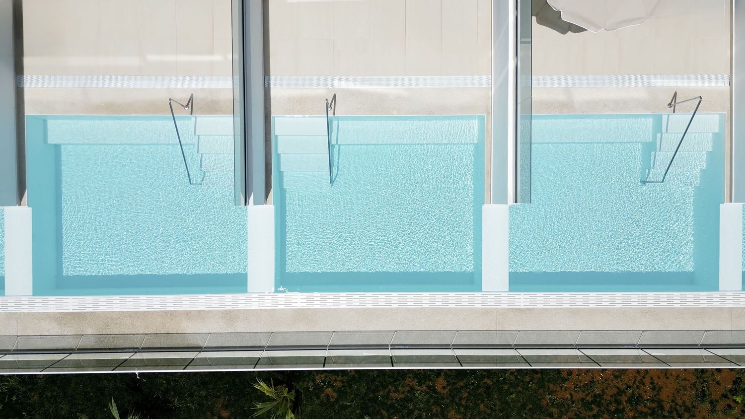 Overhead view of sleek rectangular swimming pools with modern glass barriers and white supports on a luxury building.