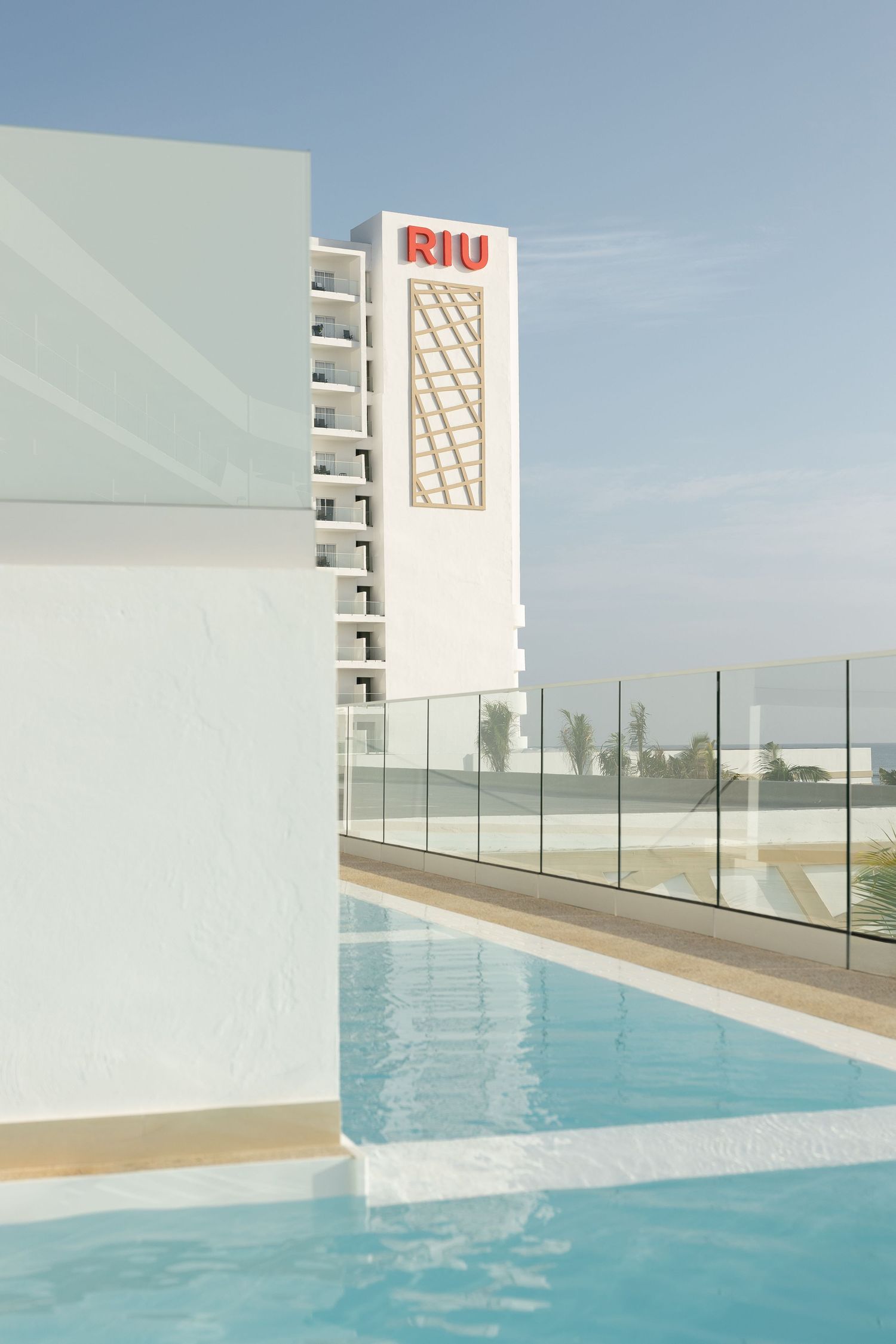 Modern white RIU hotel building with rooftop swimming pool and glass barriers.
