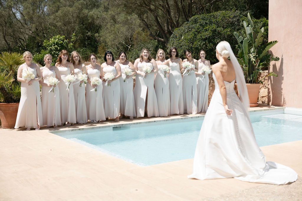 Large bridal party in matching pale gray dresses lined up by a pool.