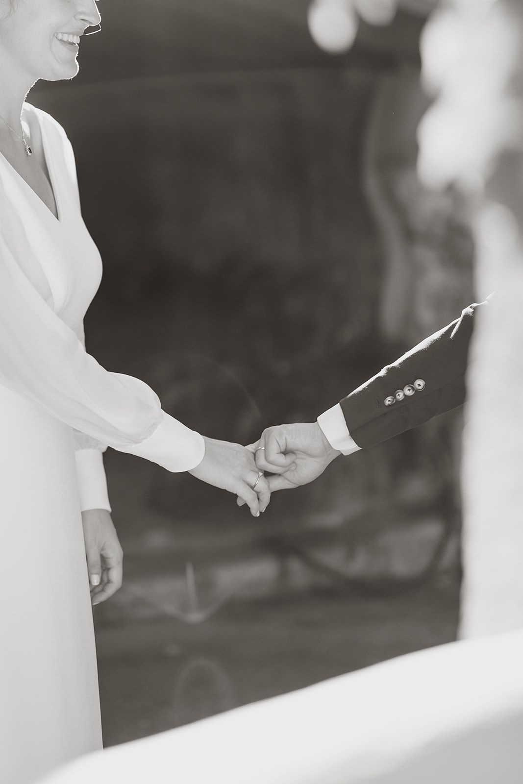 Black and white close-up of couple holding hands during wedding ceremony.