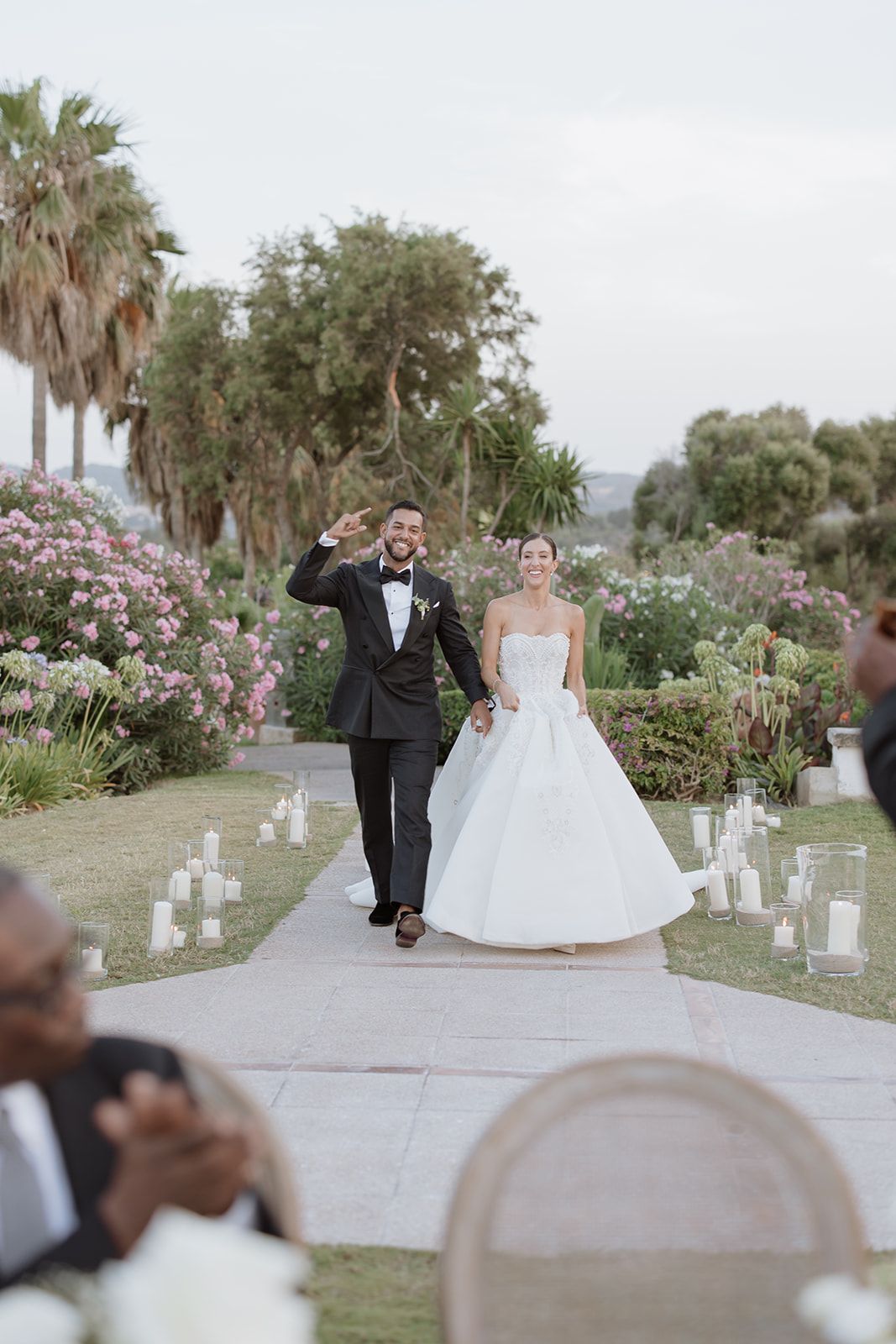 Wedding ceremony pathway lined with candles and palm trees in a romantic garden setting.