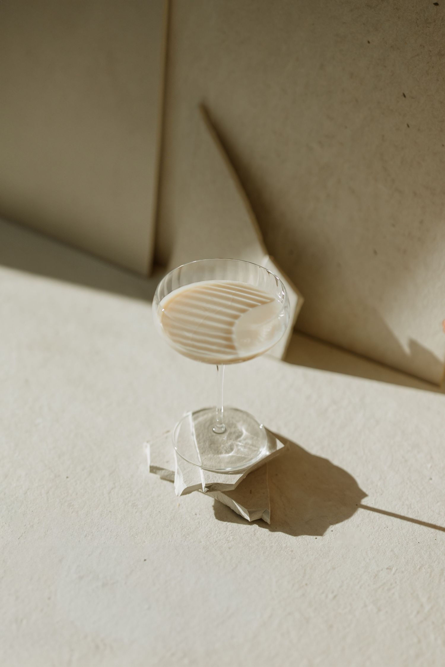 A cocktail glass casting dramatic shadows on a white surface in natural light.