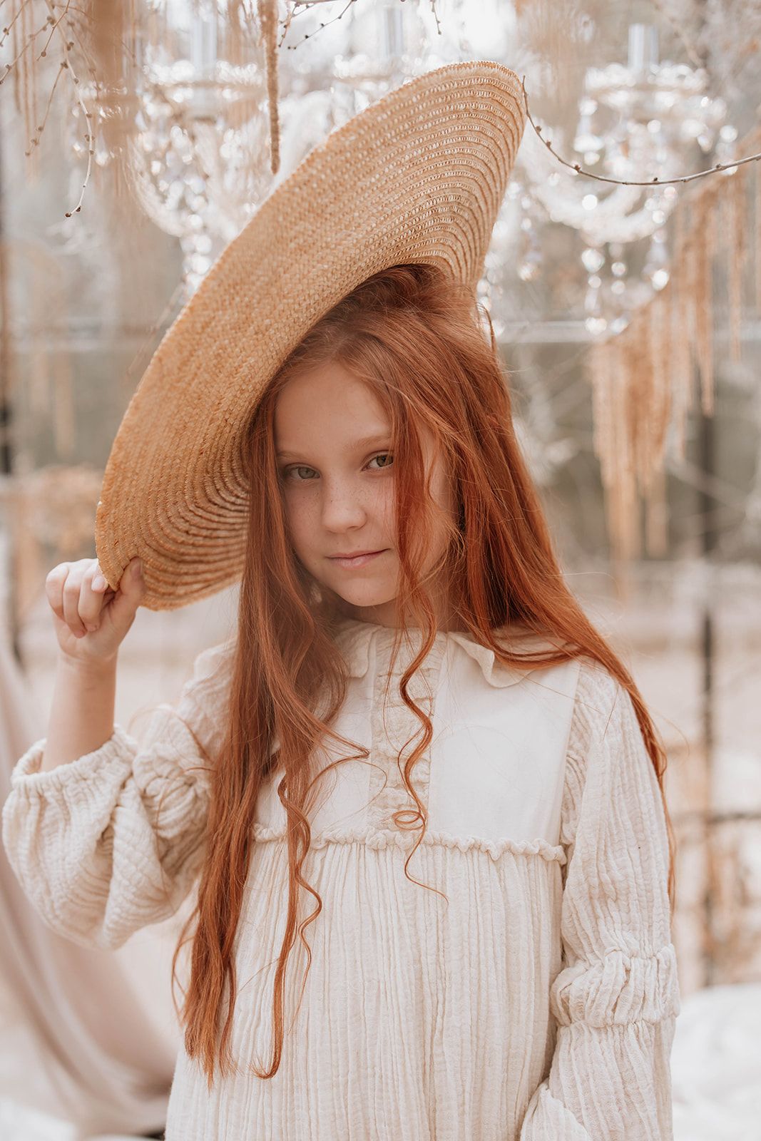 Long red hair and straw hat create a vintage aesthetic against a dreamy winter backdrop.
