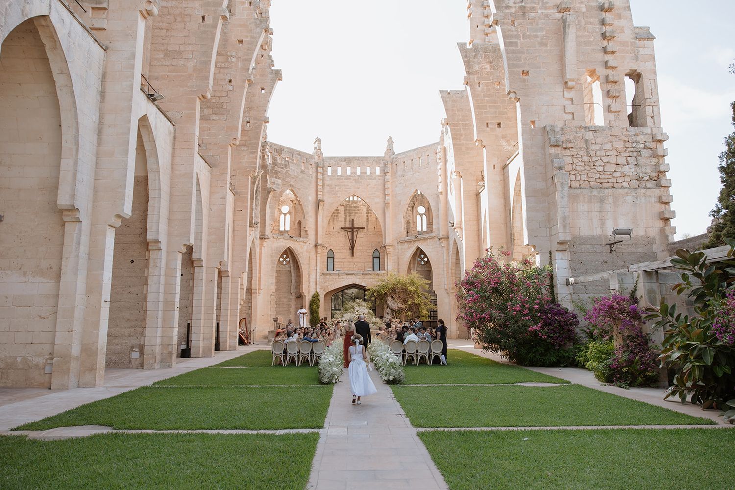 Wedding ceremony setting with white chairs arranged on green lawn inside historic church ruins.