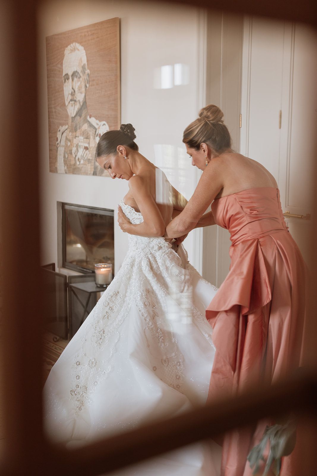 Behind-the-scenes moment of wedding dress preparation with bridesmaid helping with final adjustments.