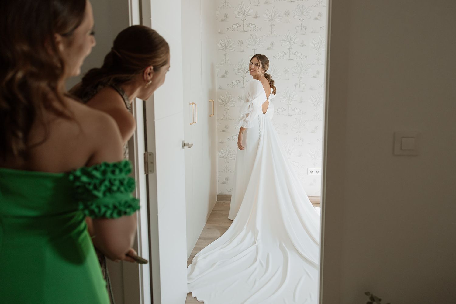Wedding dress reveal moment captured through doorway with onlookers in foreground.