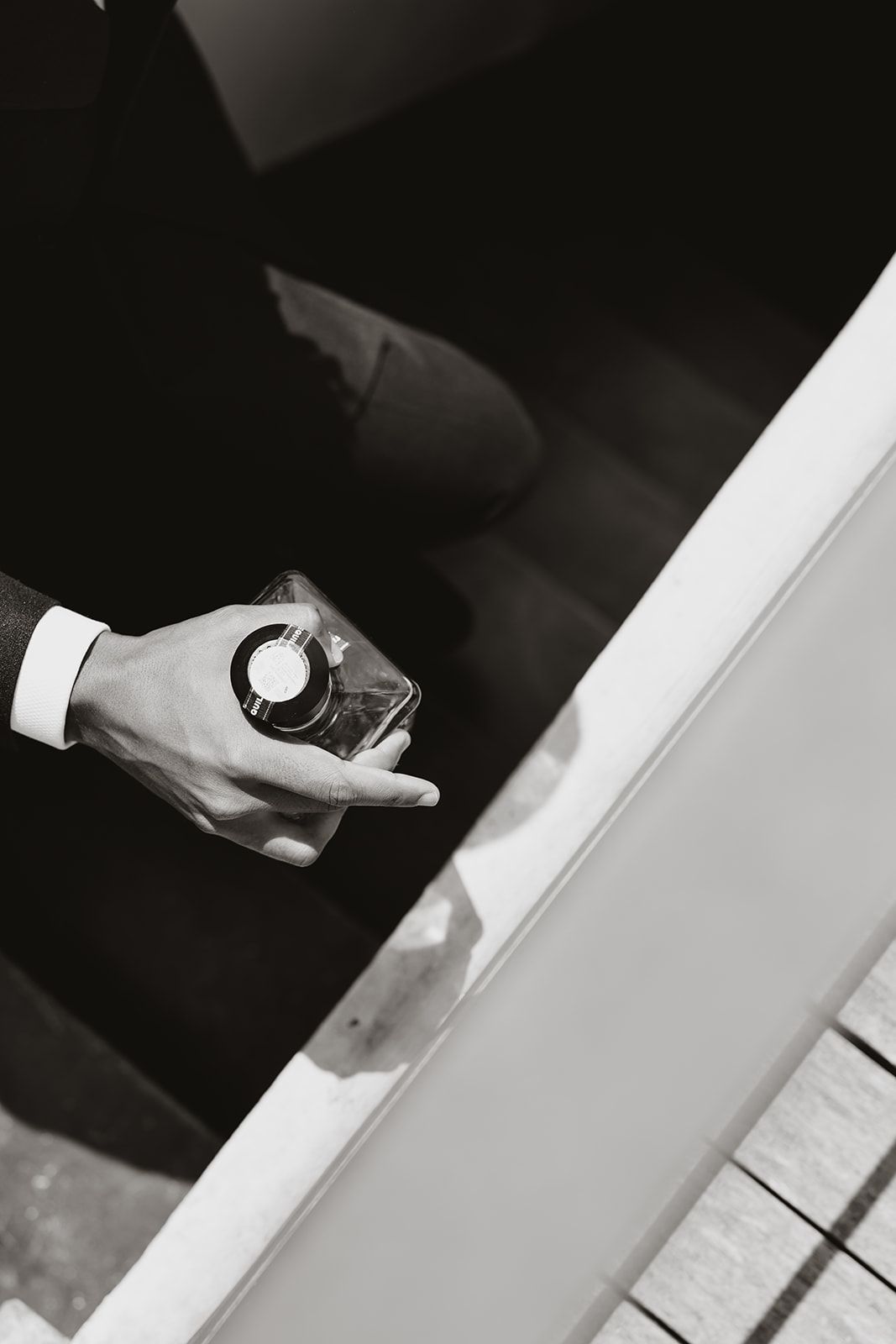 Black and white close-up of hand holding glass bottle.