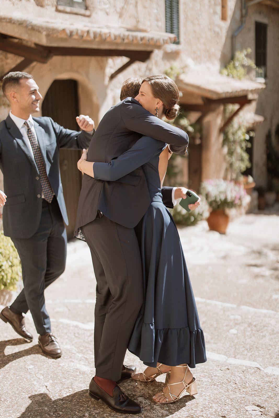 Wedding guests sharing emotional embrace in Mediterranean courtyard.