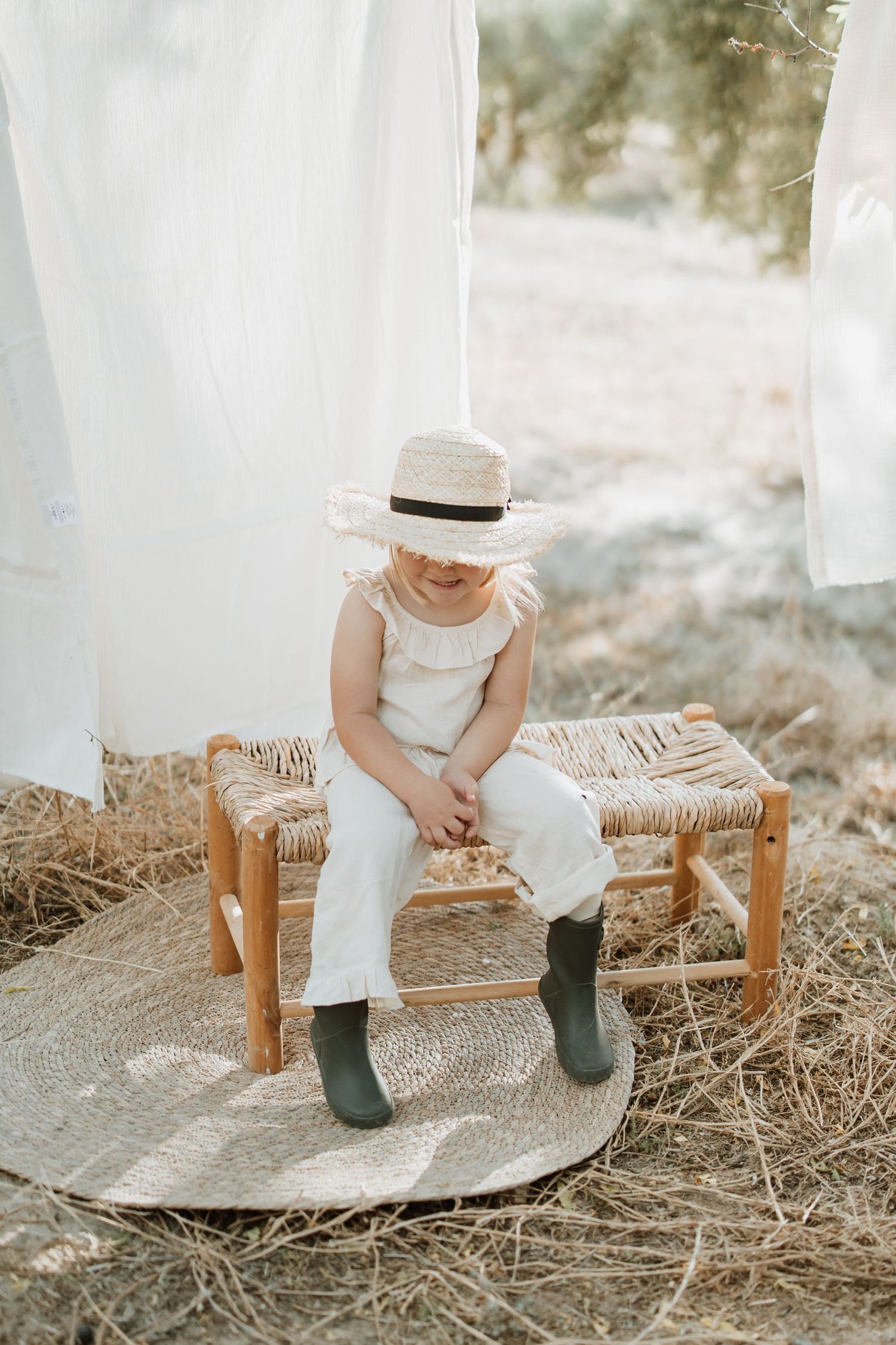 Vintage-inspired outdoor scene with woven bench, white linens, and hunter green boots.