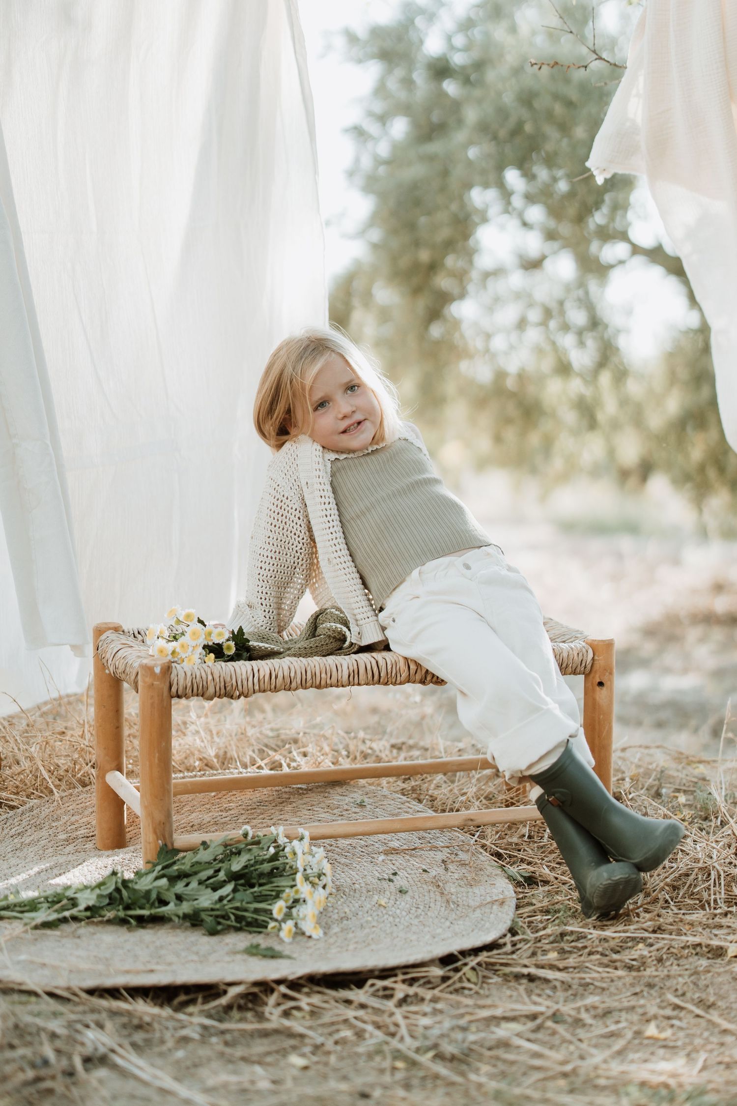 Figure sits cheerfully on rustic bench with flowers against white fabric backdrop.