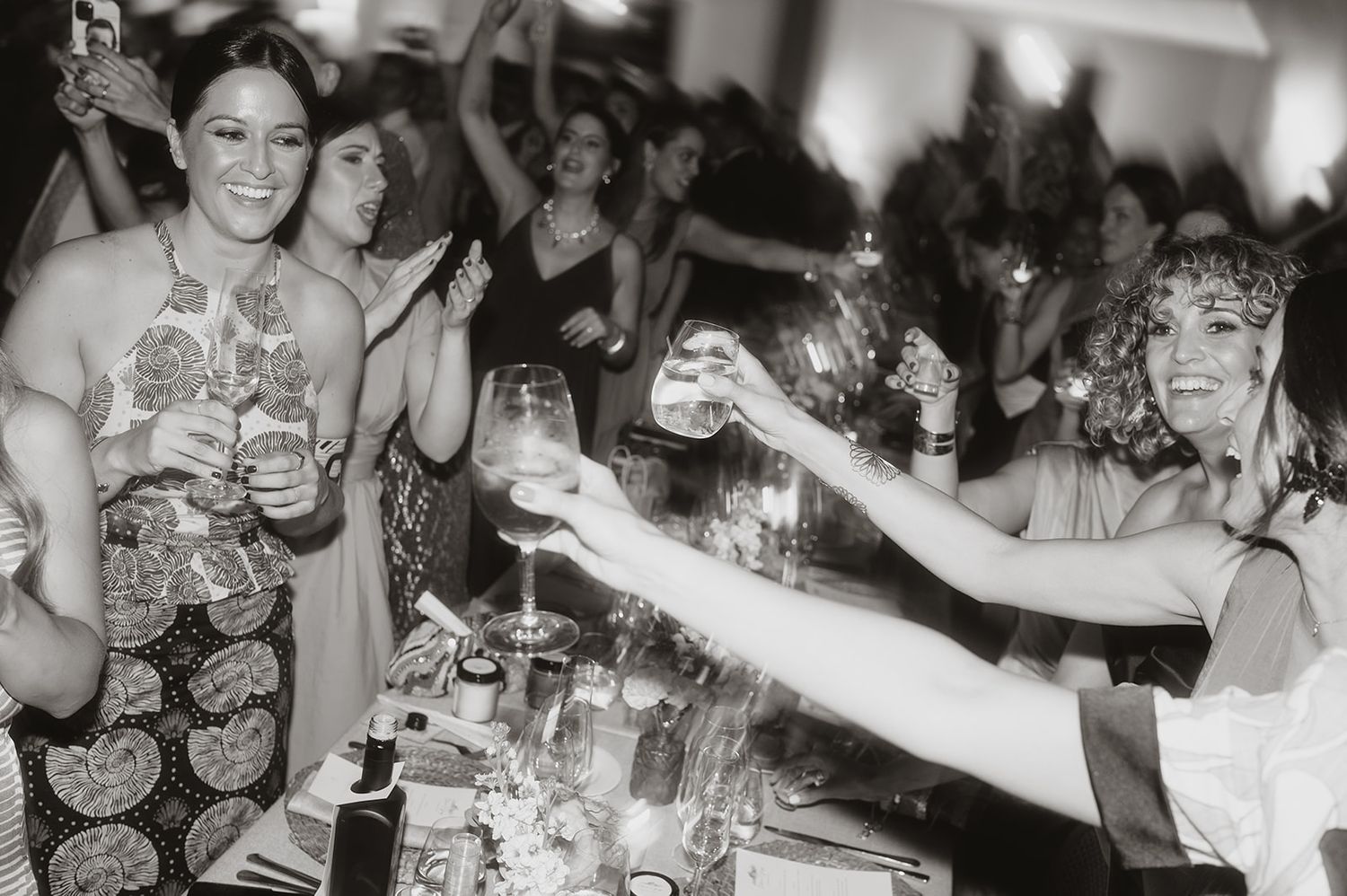 Vintage black and white photo of wedding guests raising glasses in celebration at a reception.