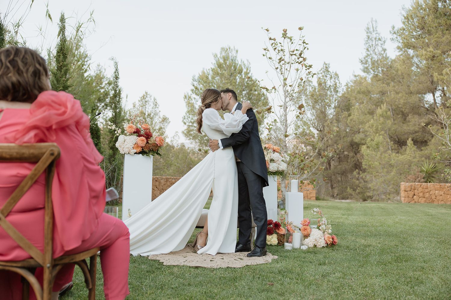 A wedding couple sharing their first kiss at an outdoor ceremony with floral decorations.