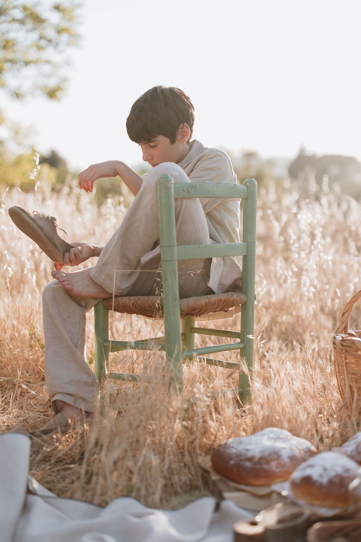 A person reads a book while relaxing on a mint green wooden bench surrounded by golden tall grass at sunset.