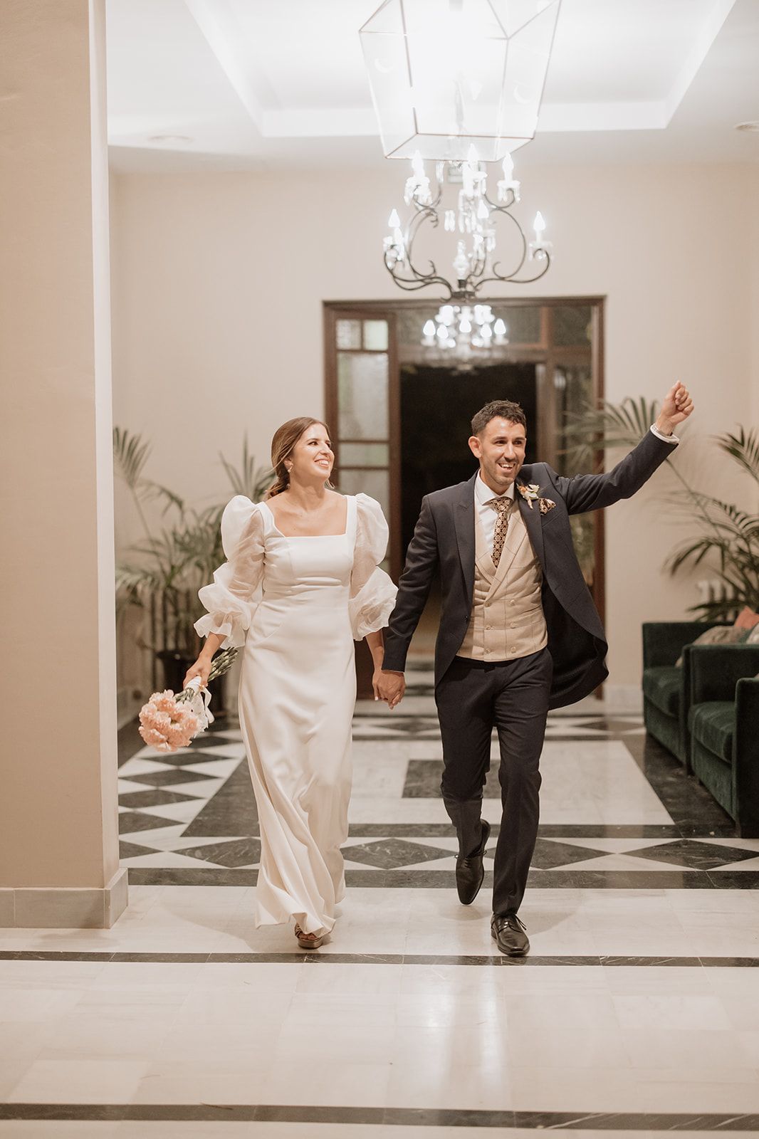 A couple joyfully walking down an elegant hallway after their wedding ceremony.