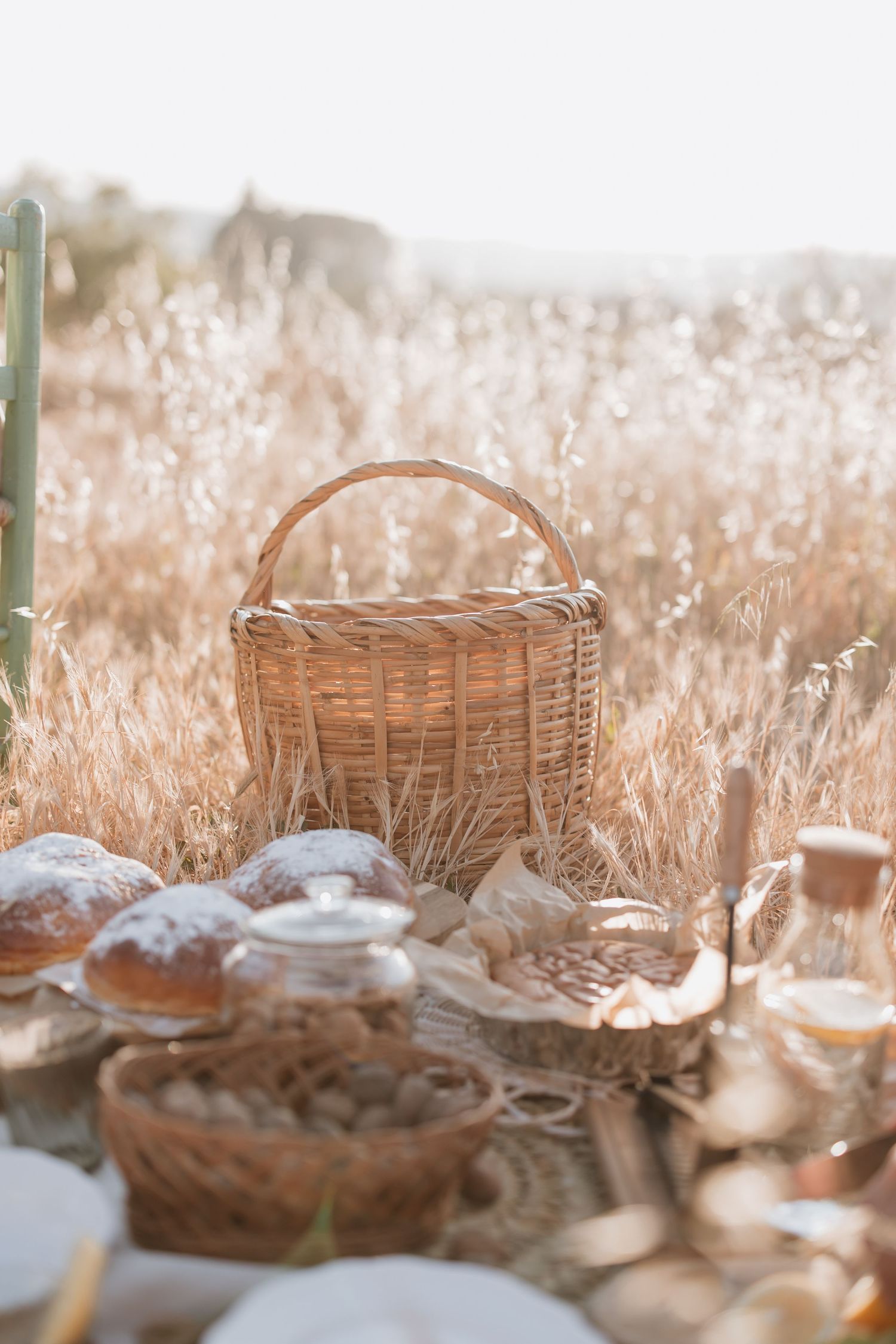 Rustic wicker picnic basket surrounded by artisanal breads on a blanket in a sunlit meadow with golden grass.