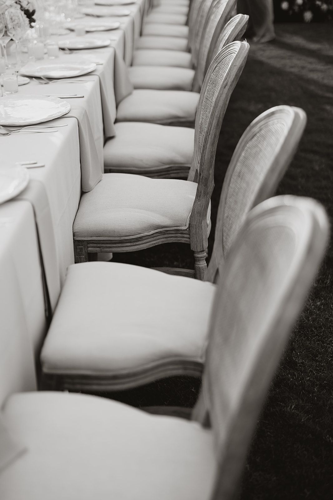 Elegant white upholstered dining chairs lined up along a formal table setting in a monochromatic style.