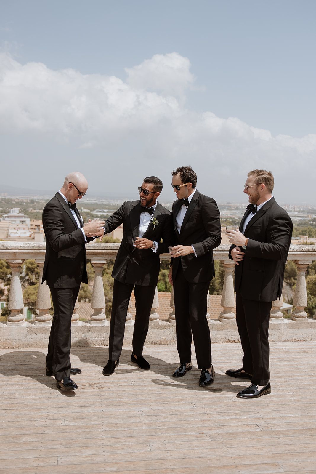 Group of formally dressed people chatting on balcony with city view.