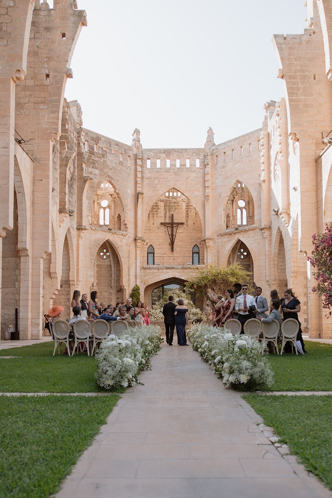 Wedding ceremony setup in a Gothic stone castle courtyard with white floral aisle decorations.