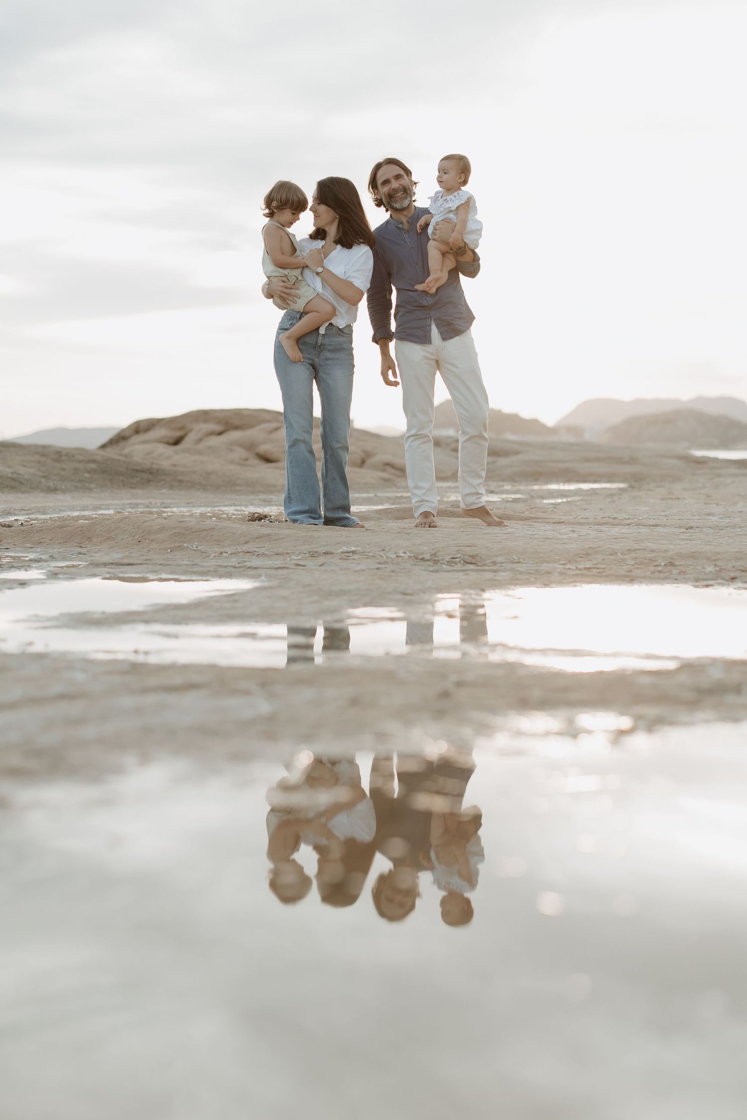 Family members reflected in coastal water pools at sunset.