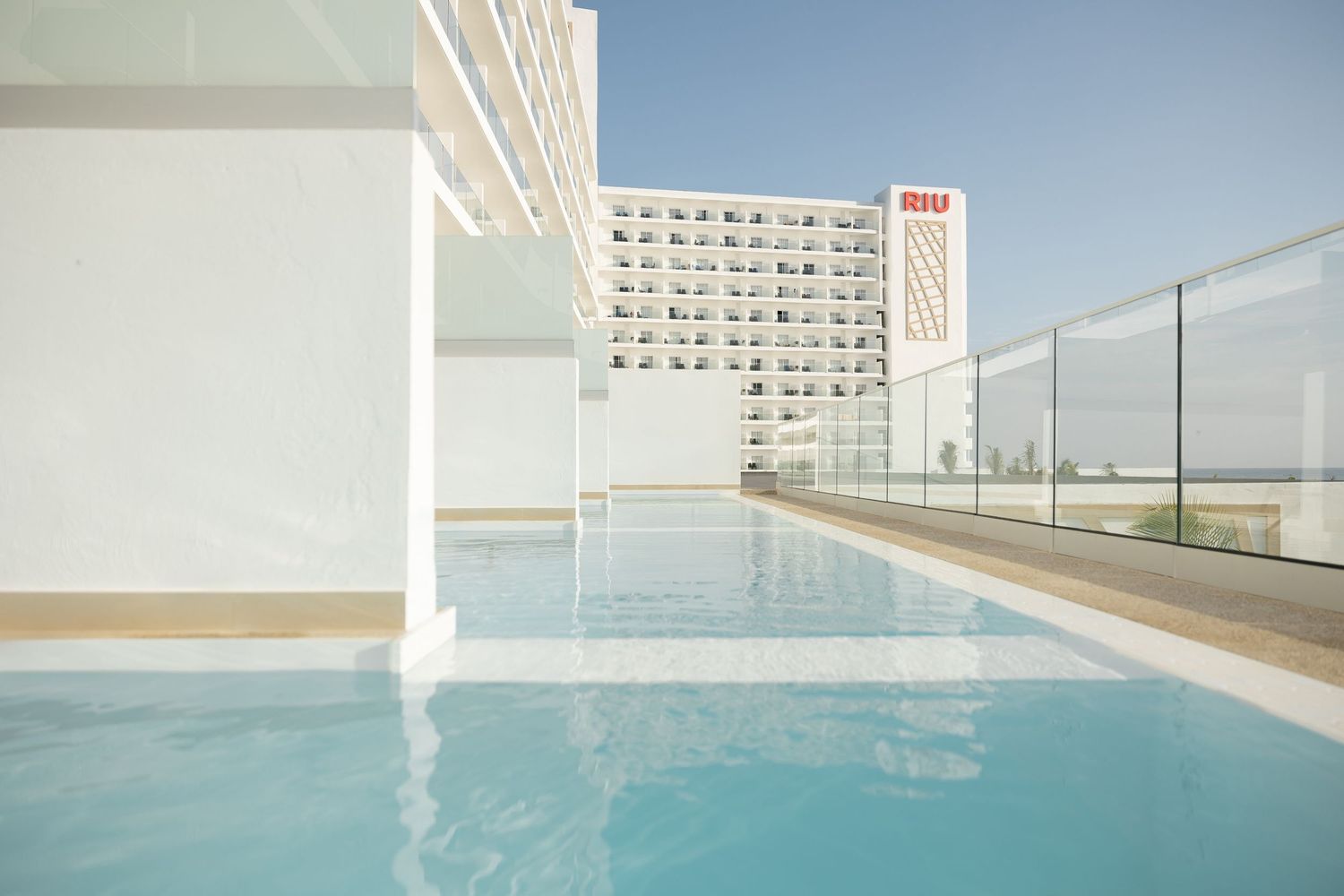 Rooftop swimming pool with glass barriers overlooking a modern urban landscape.