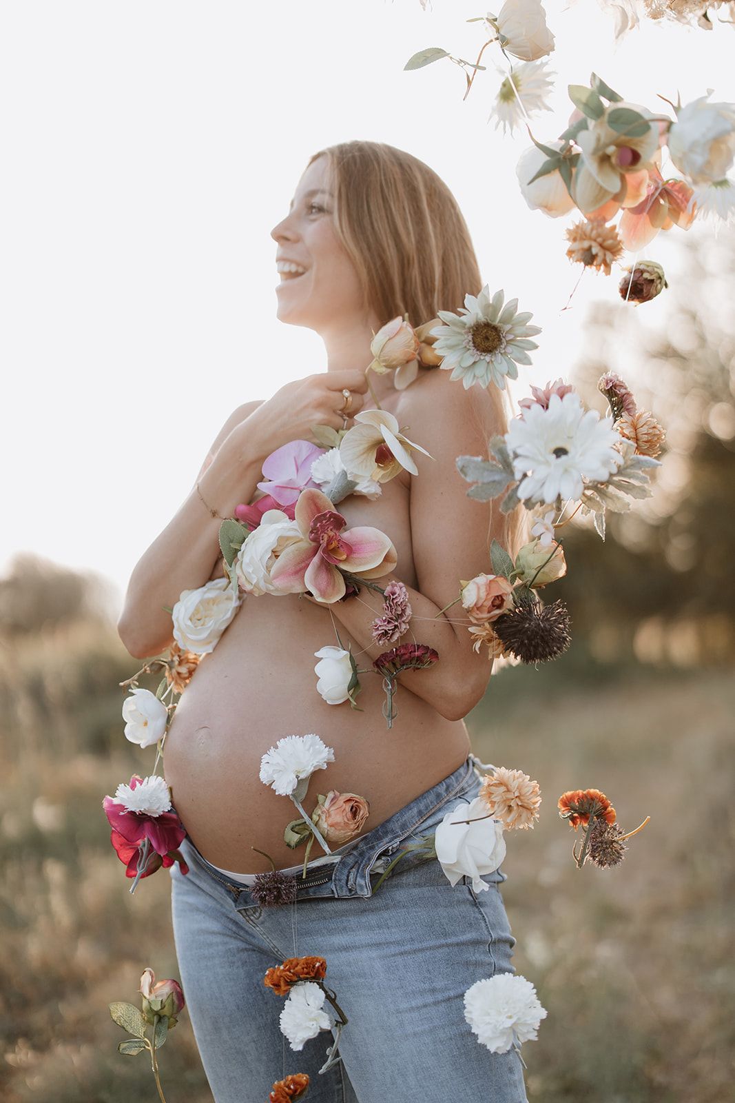 A joyful maternity portrait with flowers arranged on the belly in soft natural lighting.
