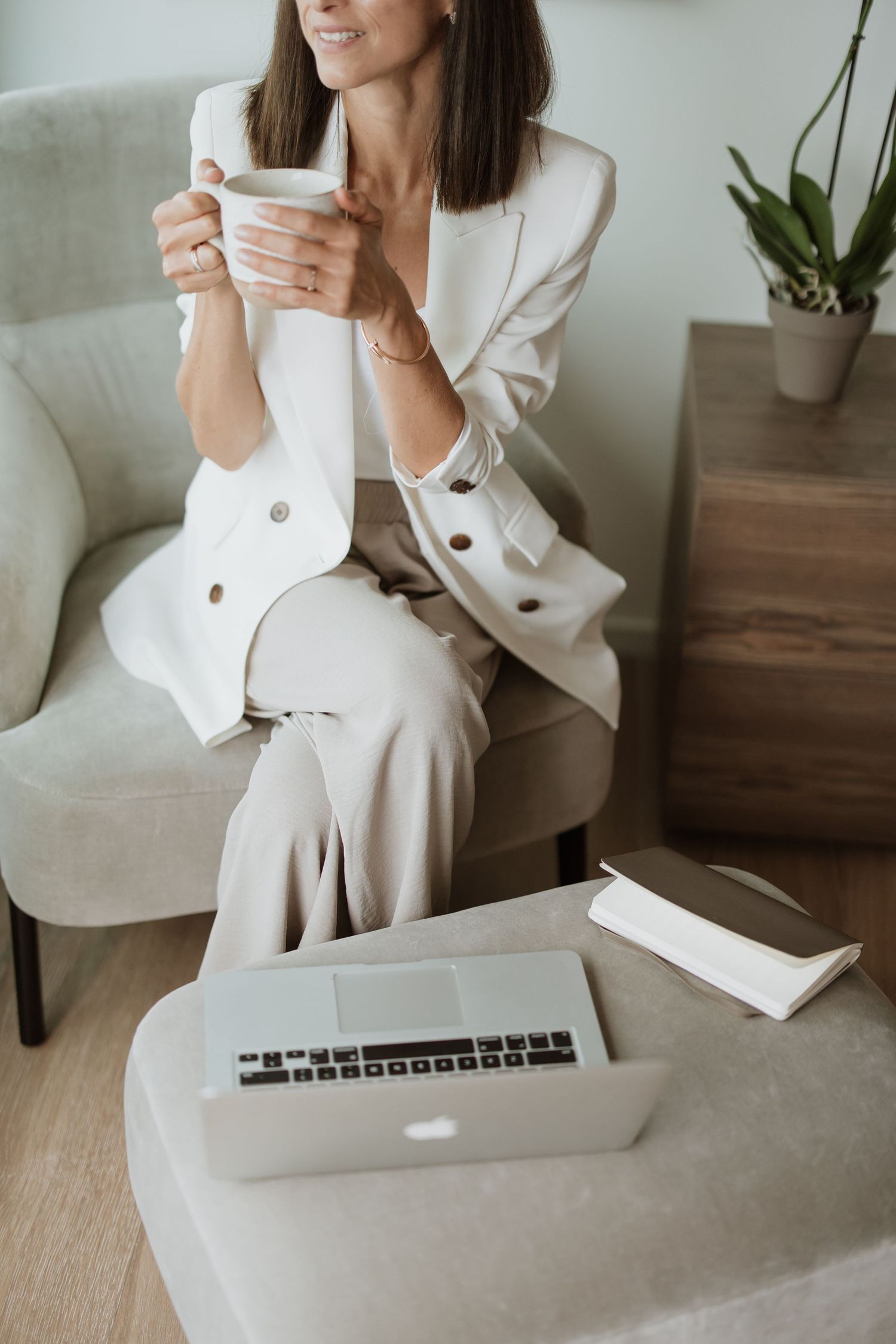 Person working on laptop while sitting in white professional attire with coffee cup.