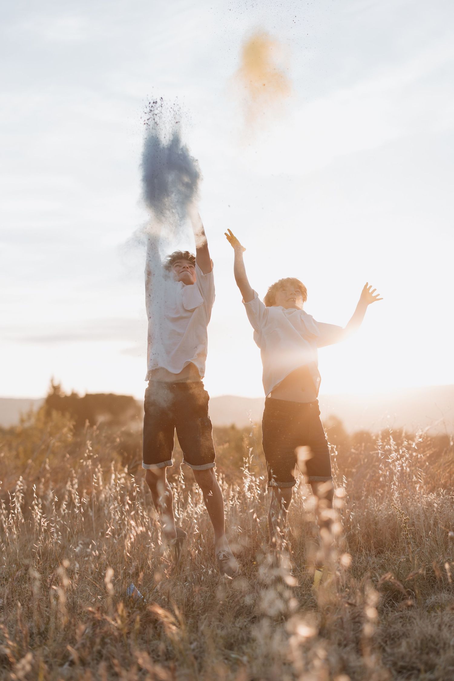 Two silhouettes jump joyfully in a sun-drenched meadow filled with tall grass during golden hour.