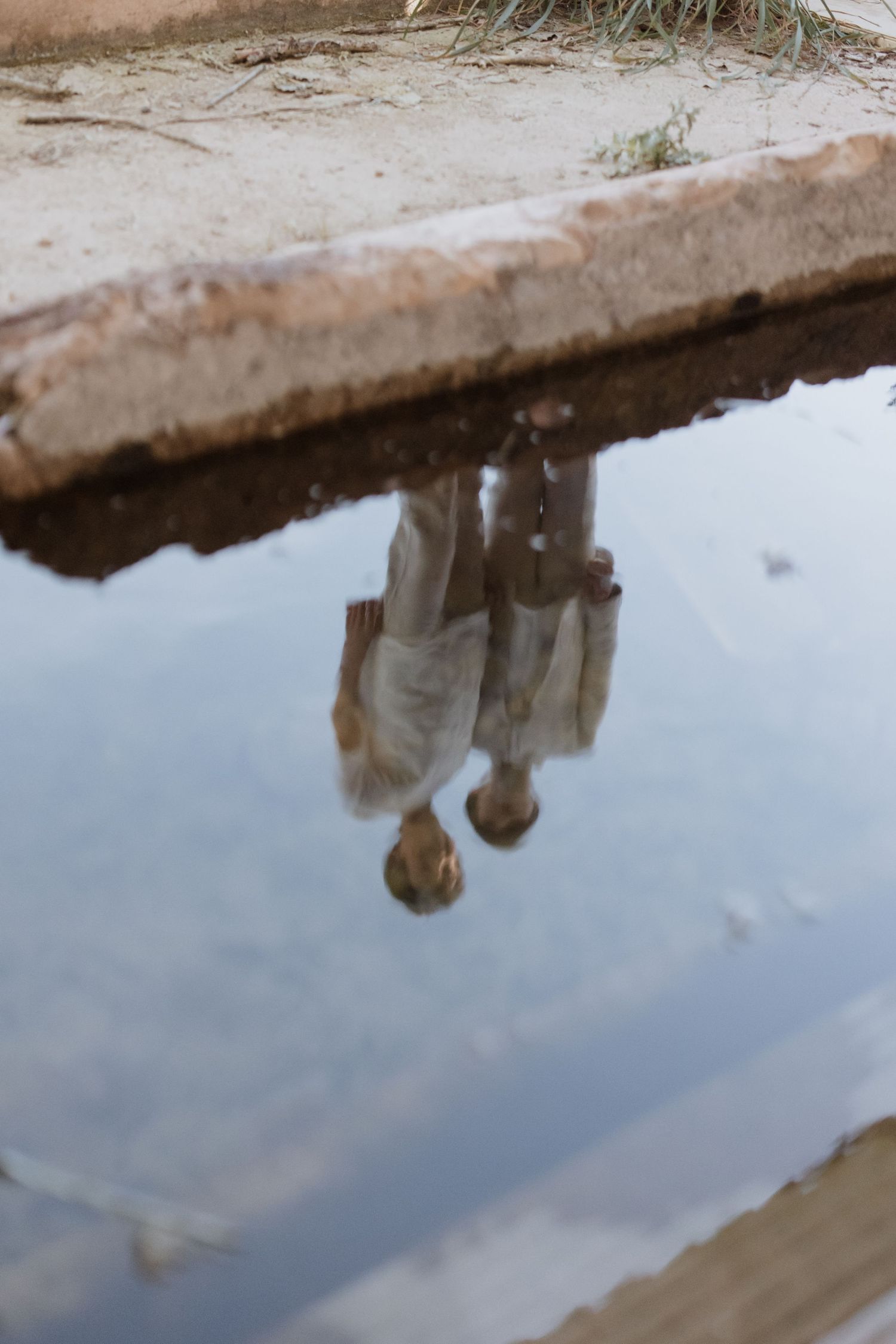 A reflection in a puddle shows a silhouetted figure against a cloudy sky.