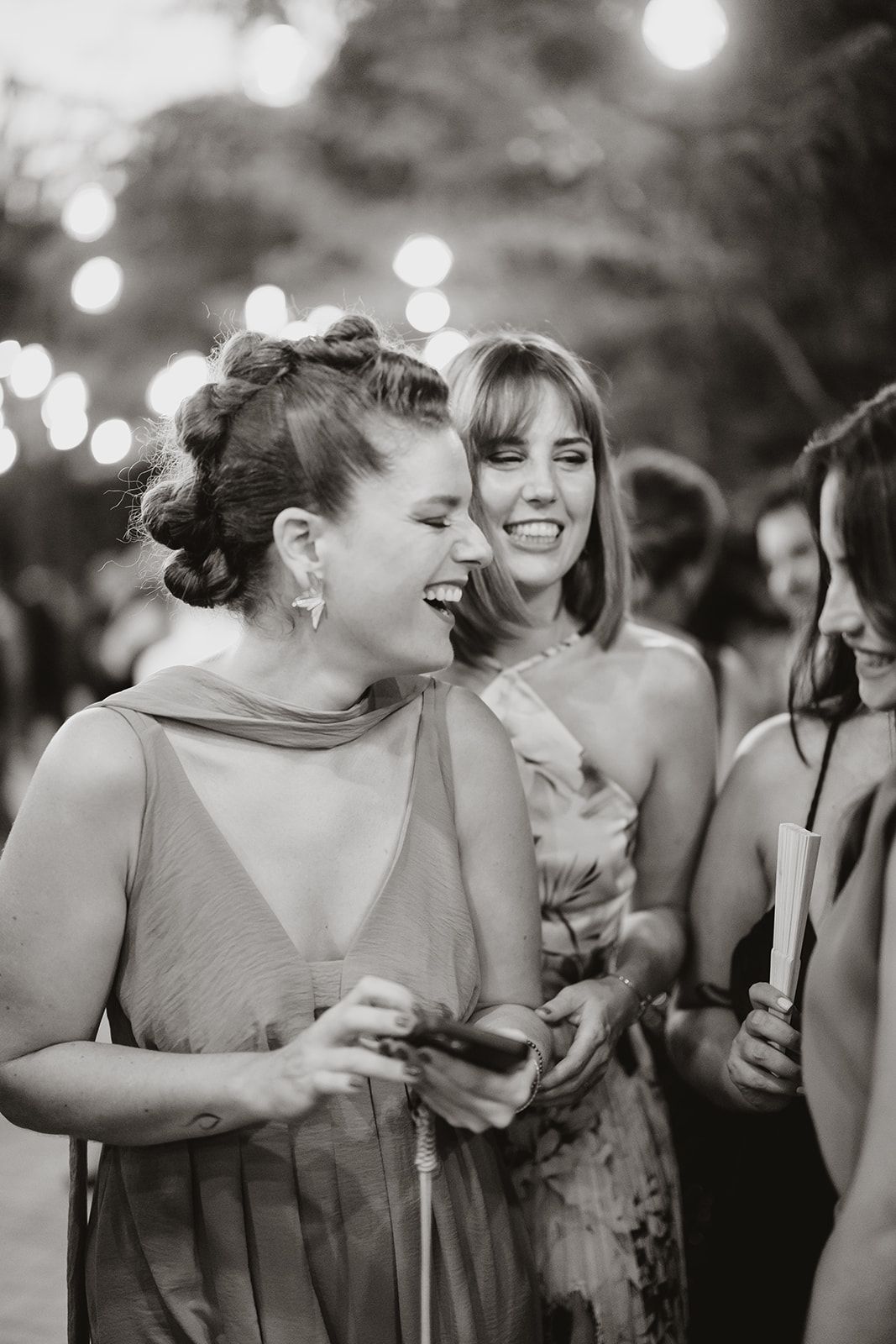 Wedding guests sharing joyful laughter during an evening celebration with bokeh lights.