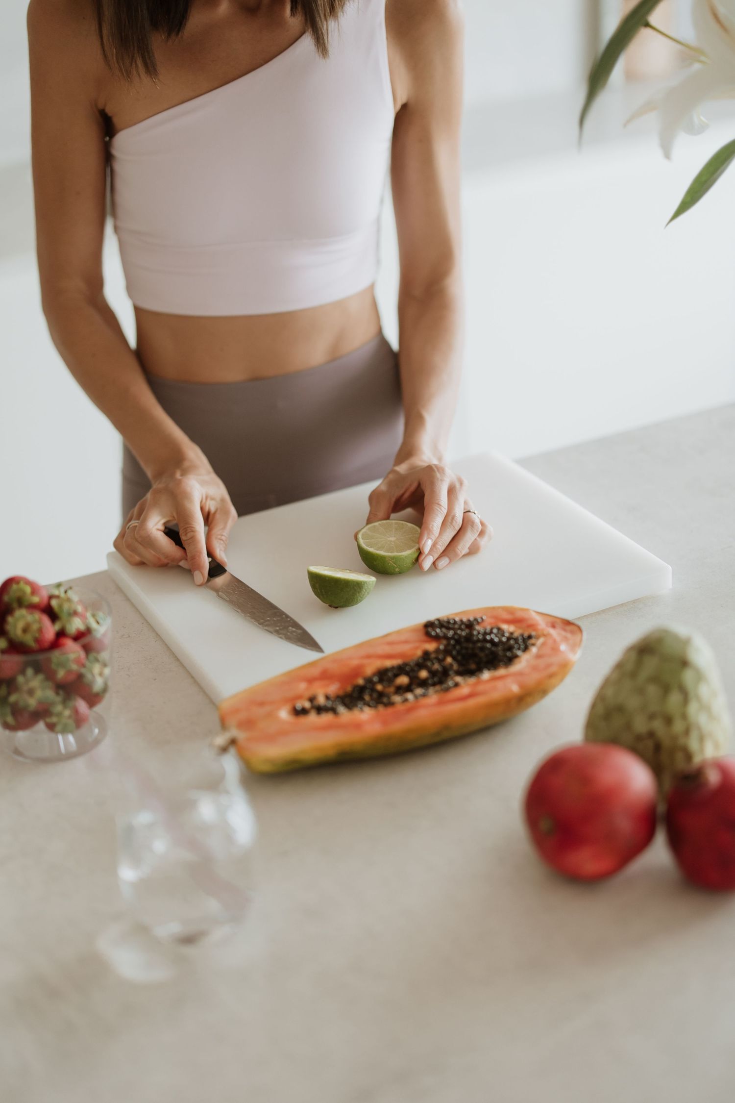 Fresh papaya and fruits being prepared on white cutting board in minimalist kitchen.