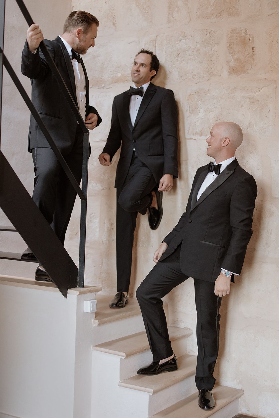 Three men in tuxedos arrange themselves casually on interior stairs for a photo.