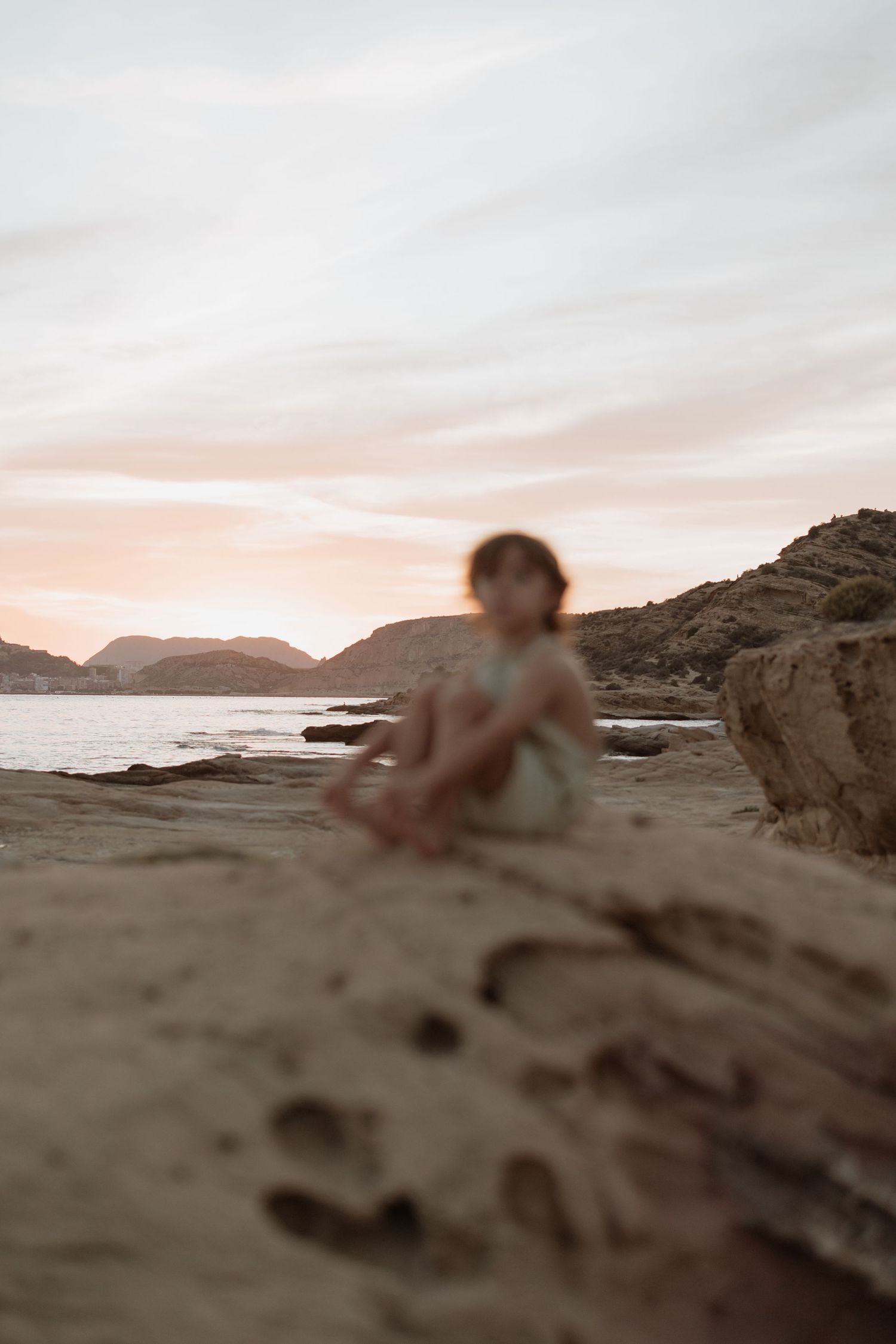 Dreamy coastal landscape with figures on rocks during pink sunset.