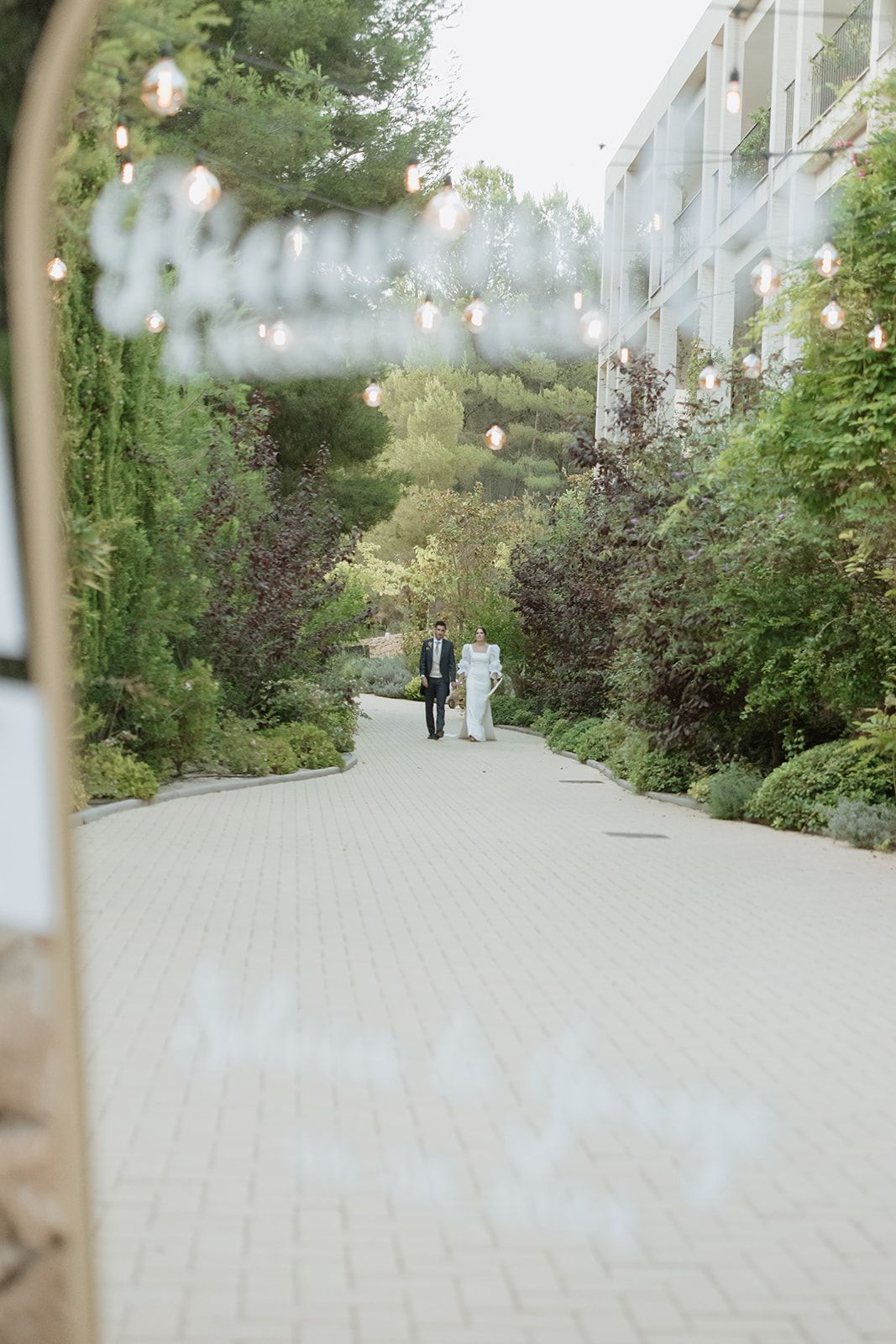 Garden pathway lined with trees and greenery leading to an outdoor wedding venue.