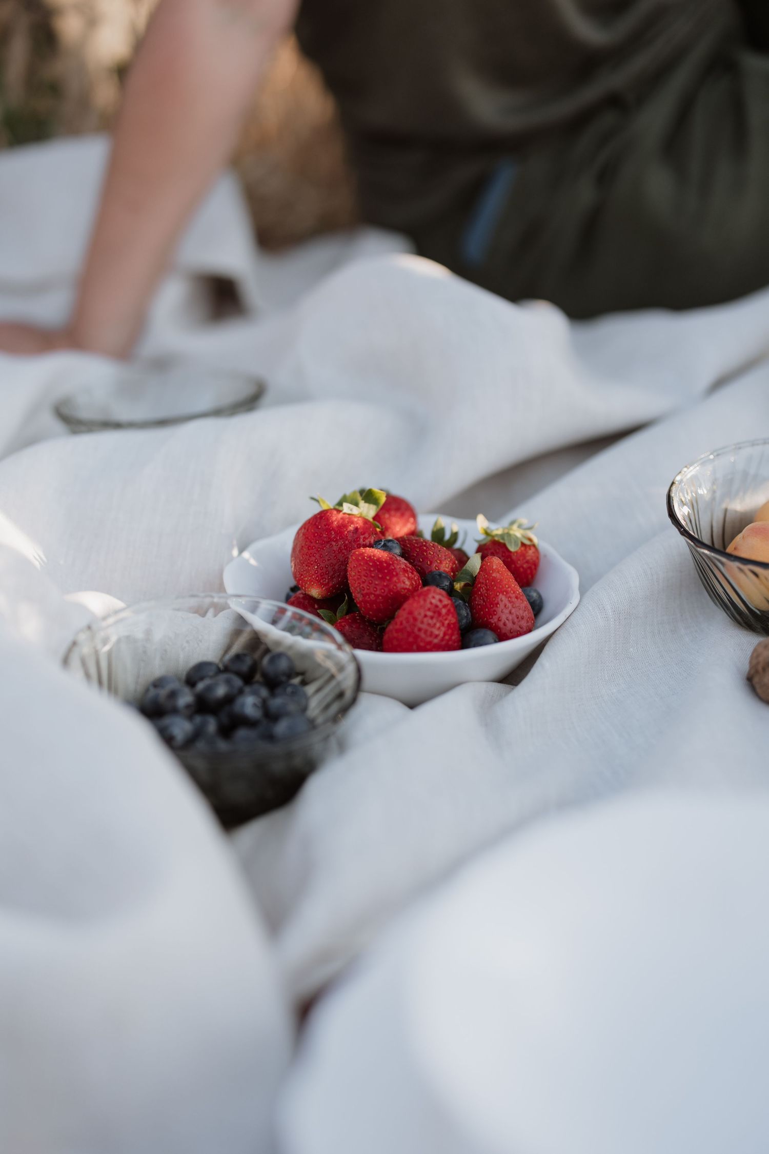 Fresh red strawberries and blueberries served in white bowls on a light linen tablecloth for a summer picnic setting.