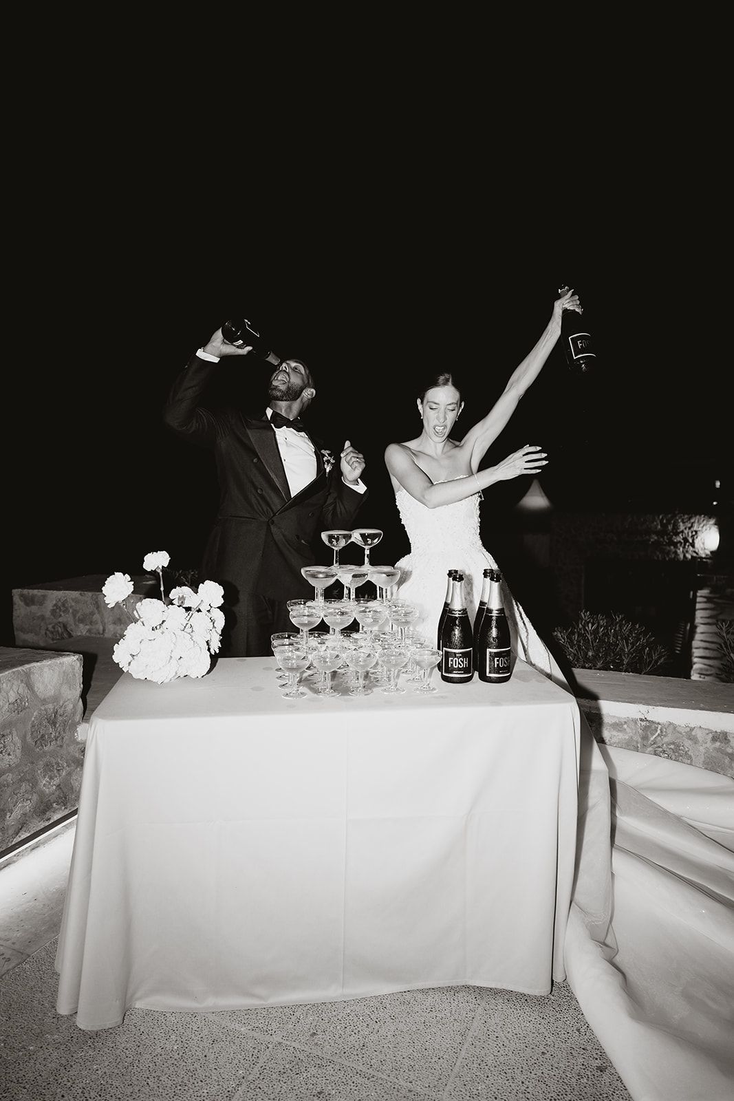 Black and white photo of a celebratory moment at a wedding champagne tower.