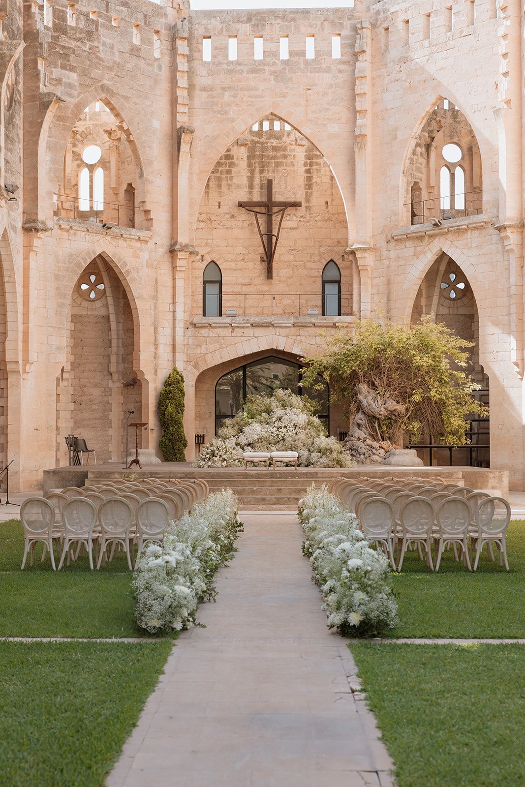 Wedding ceremony setup in a historic stone church courtyard with rows of chairs and floral arrangements.
