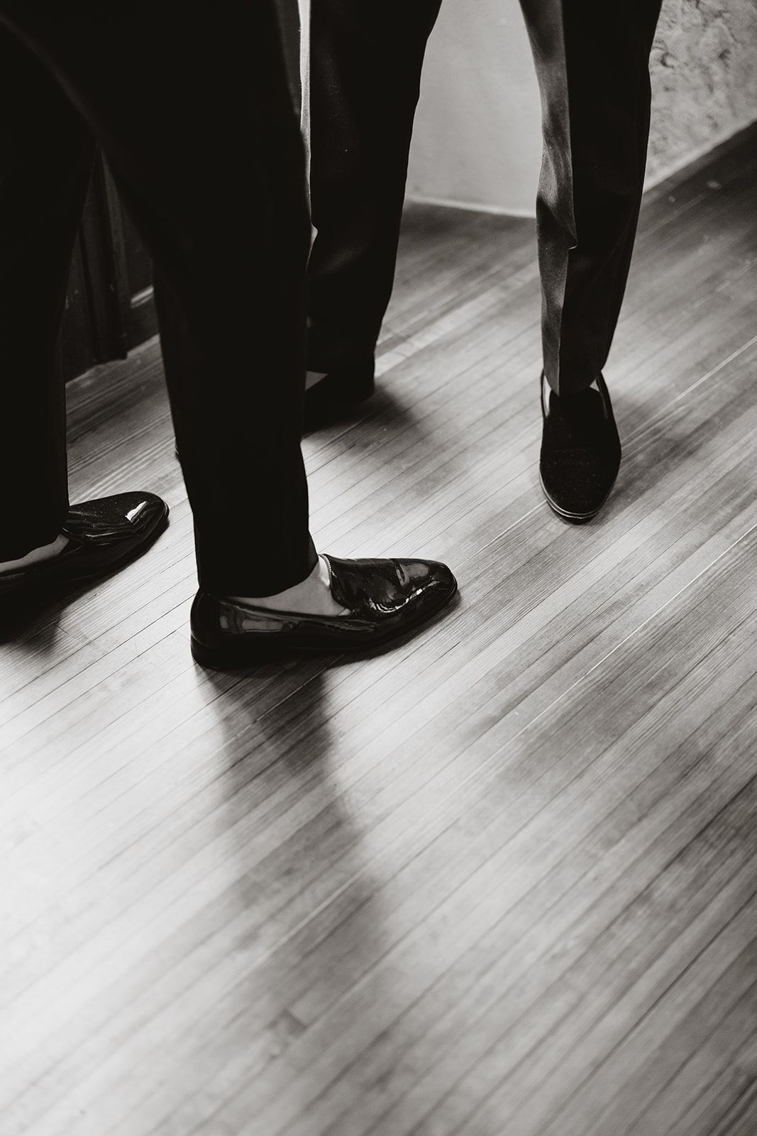Black and white detail shot of formal dress shoes on hardwood flooring.