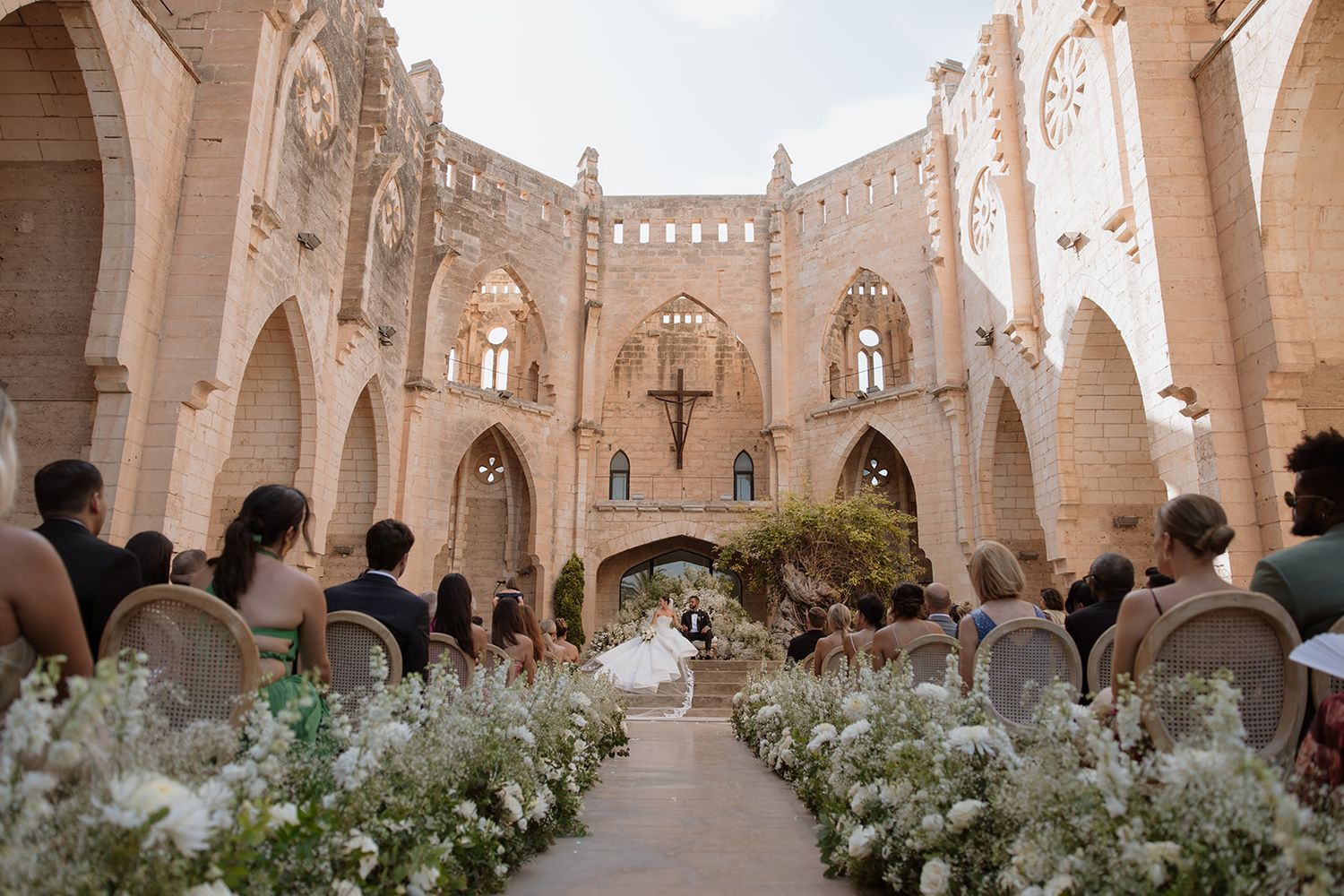Wedding ceremony setup in a stunning gothic cathedral with white floral arrangements lining the aisle.