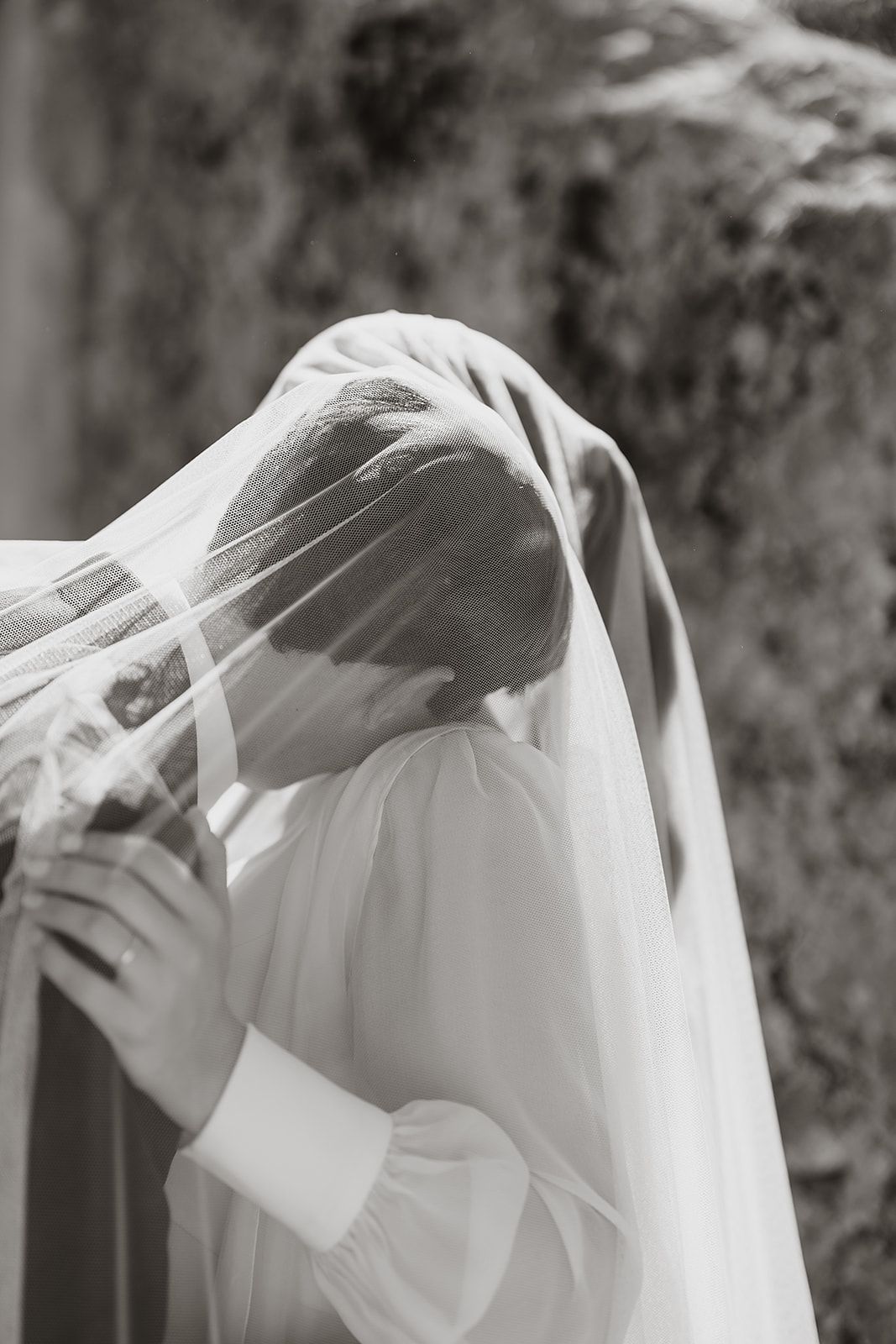 Ethereal black and white photo of a bride covered in a delicate white veil blowing in the breeze.