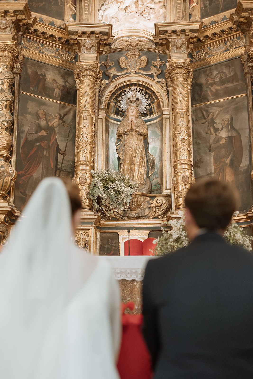 View of elaborate church altar with baroque details and religious statuary during wedding ceremony.