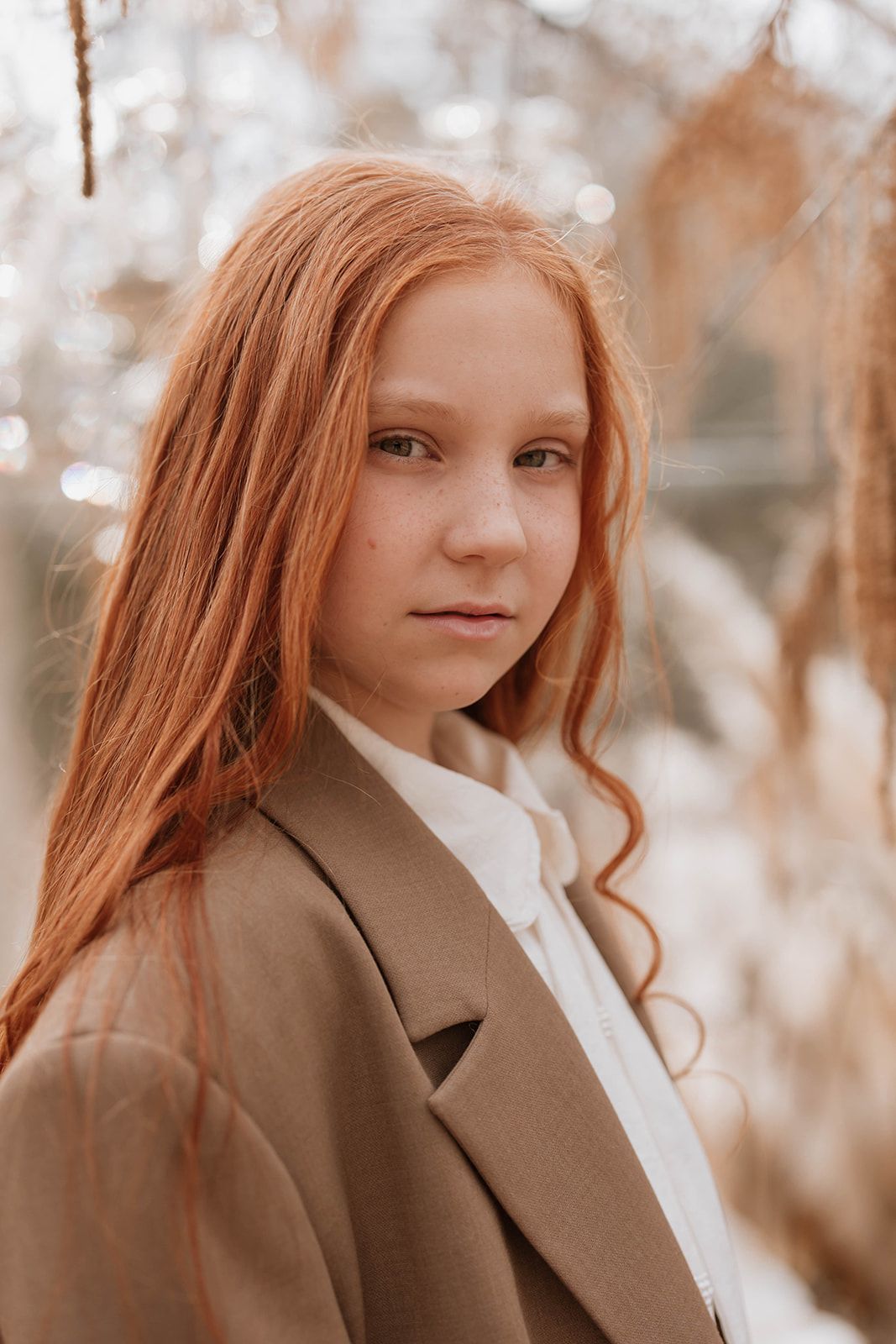A portrait in warm tones featuring beautiful long red hair and a brown coat against a soft bokeh background.
