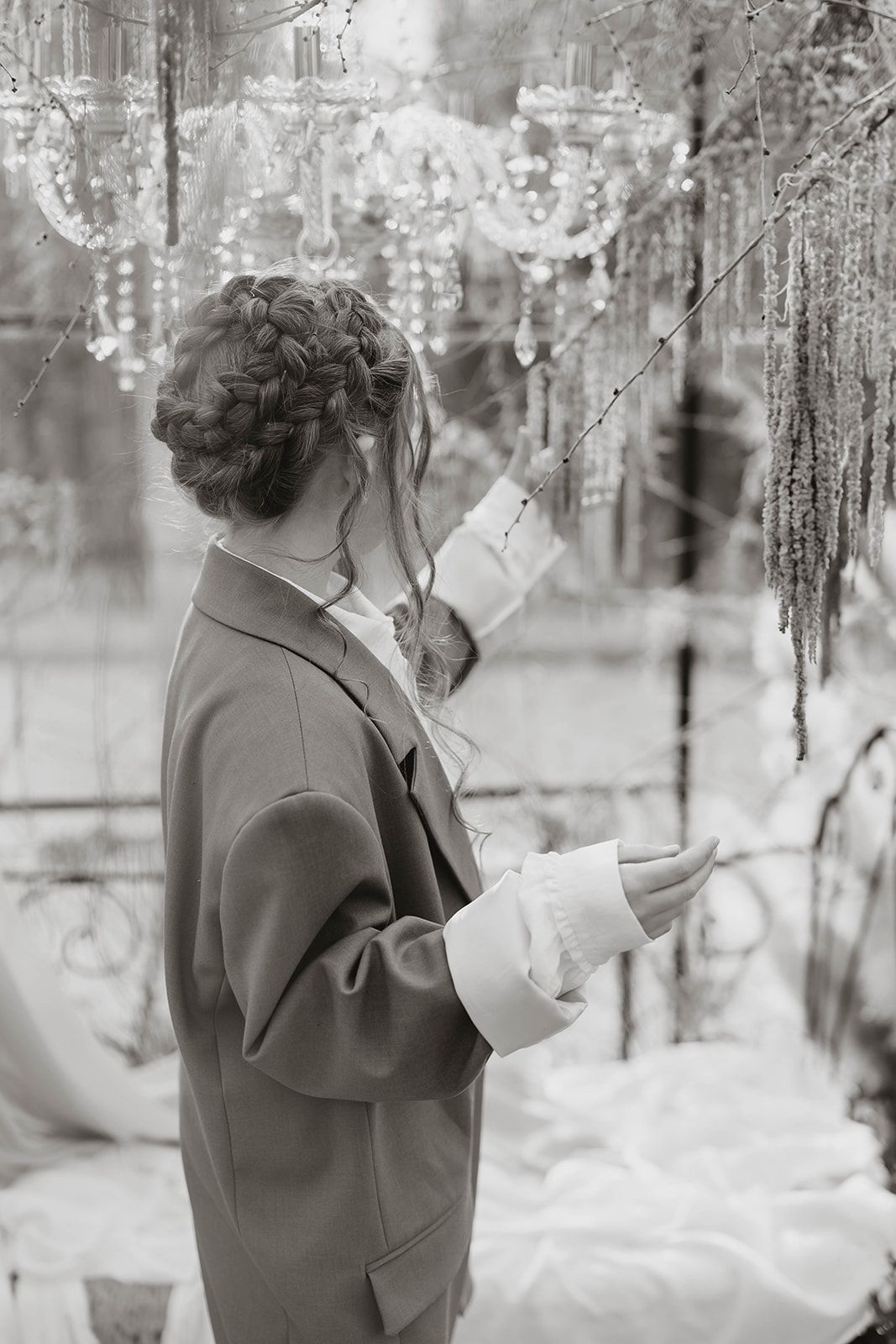 A dreamy black and white fashion portrait showing someone in a brown coat examining hanging crystal decorations.