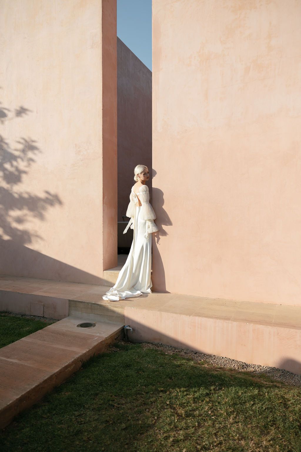 White gown with dramatic sleeves photographed against geometric architectural backdrop with grass.