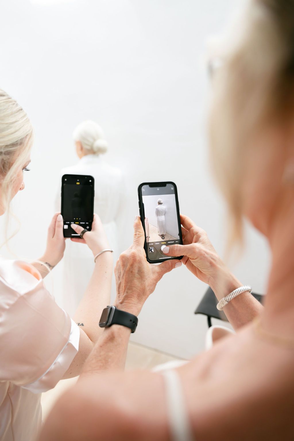 Hands holding smartphones taking pictures in a bright white room.