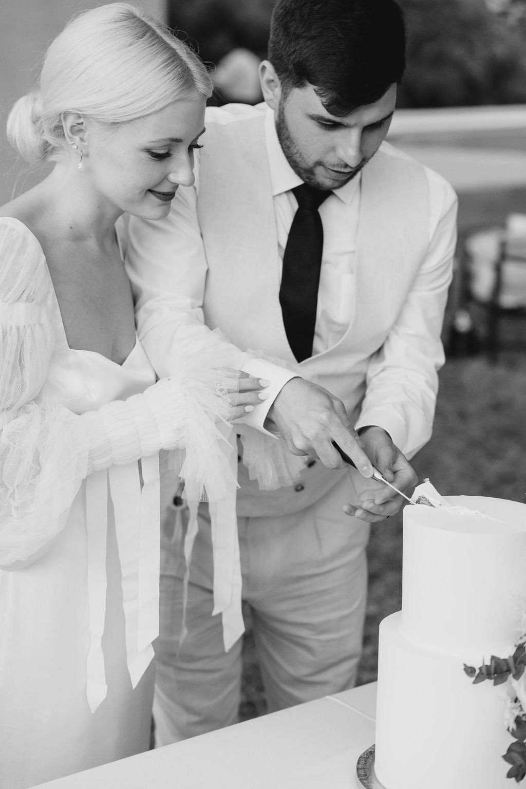 Black and white photo of newlyweds cutting their wedding cake together.
