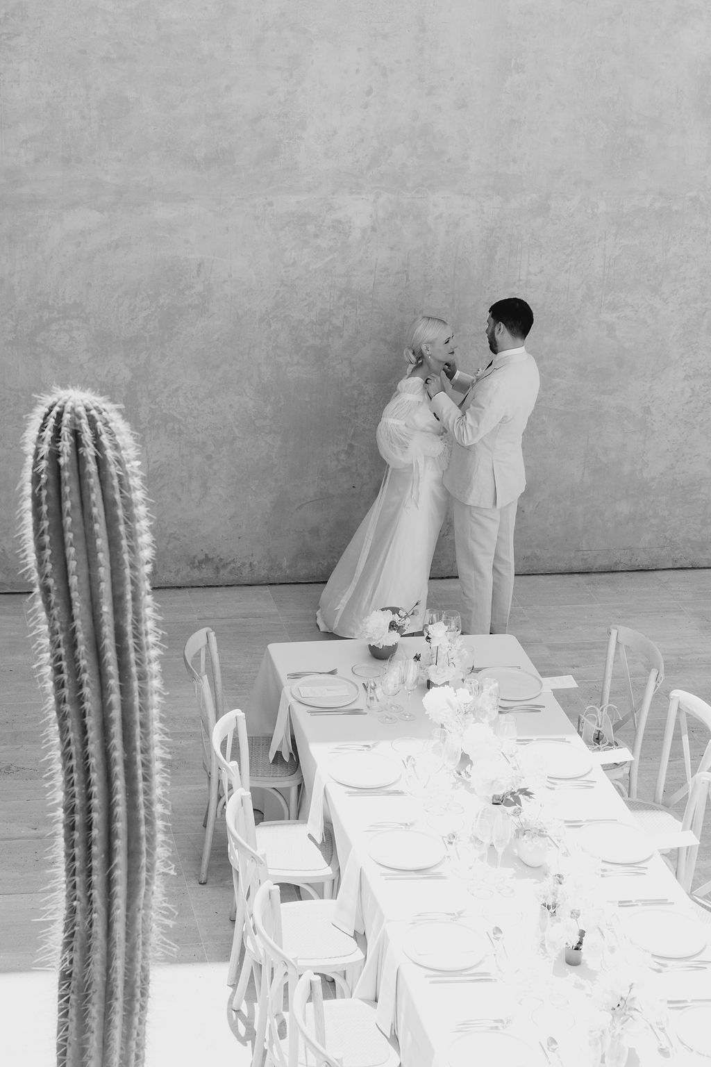 Black and white wedding photo with long dining table and tall cactus in foreground.