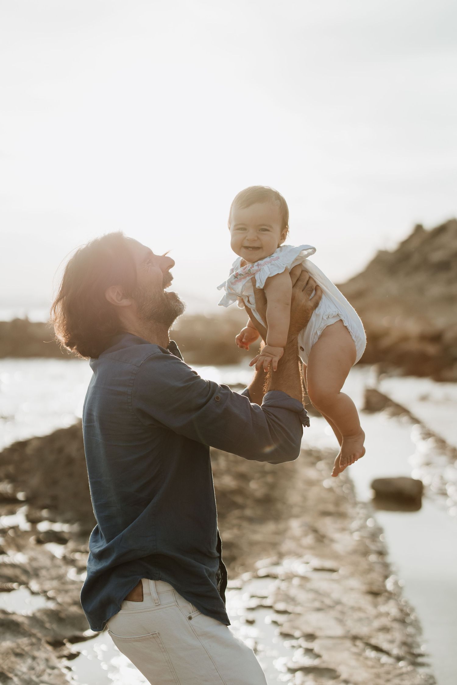 Adult and baby sharing joyful moment together on rocky beach.
