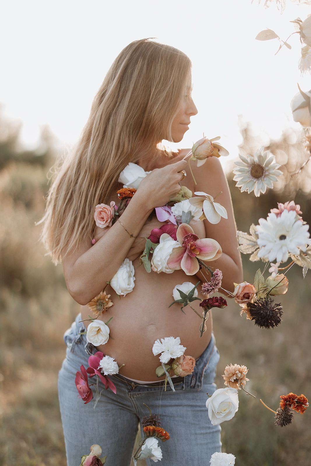 A creative maternity photo decorated with colorful flowers against the skin in golden sunlight.